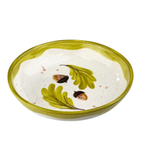 Ceramic bowl with green leaves and acorns on a white background