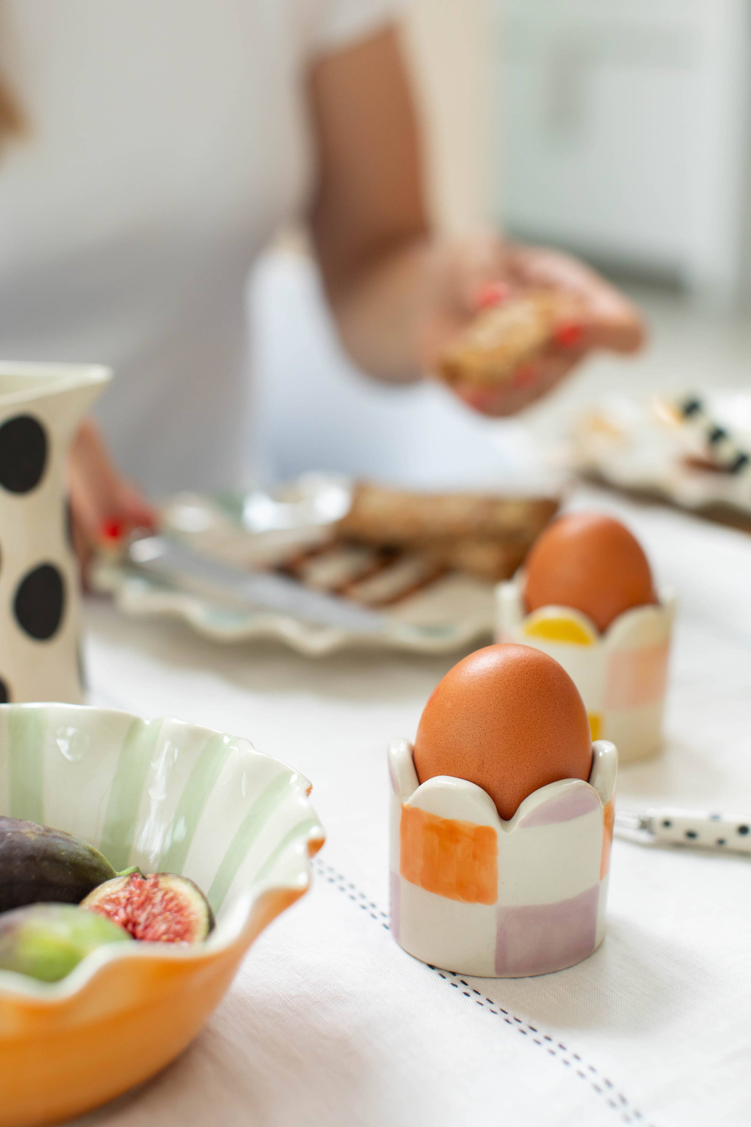 Eggs in a decorative holder on a table with a blurred background of a person and food.