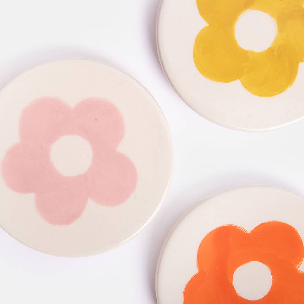 Three circular coasters with colorful flower designs on a white background