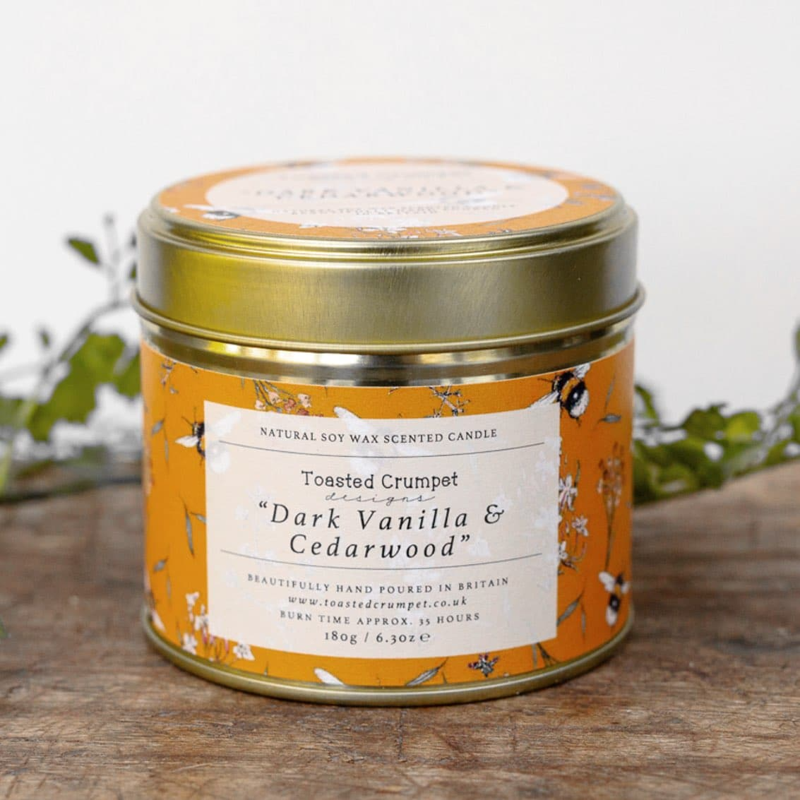 Scented candle in a decorative tin with a label on a wooden surface.
