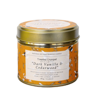 Scented candle in a decorative tin with a label on a wooden surface.