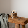 Candle with 'St EVAL' branding on a rustic wooden bench with plain background