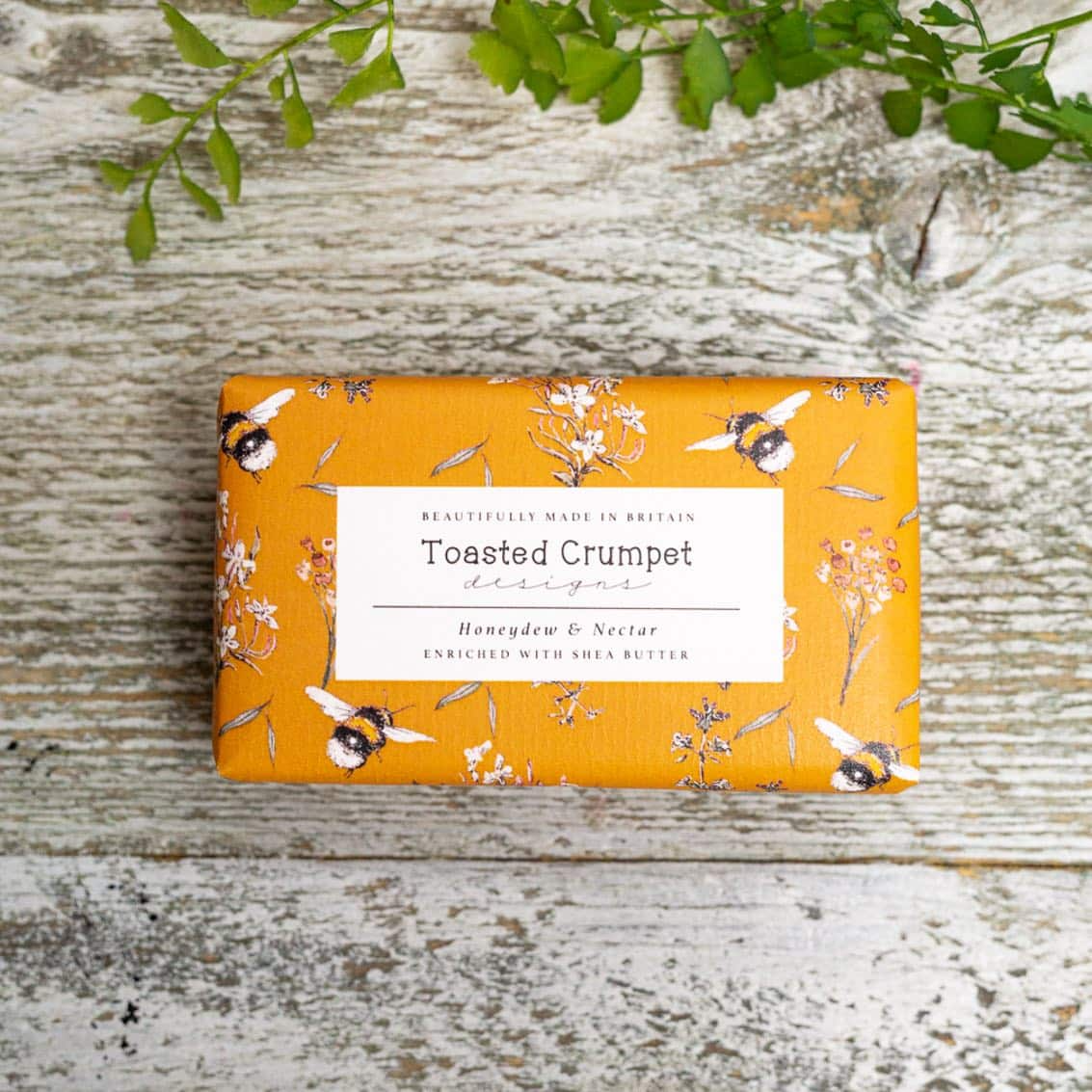 Bar of soap with decorative packaging featuring bees and flowers on a wooden surface.