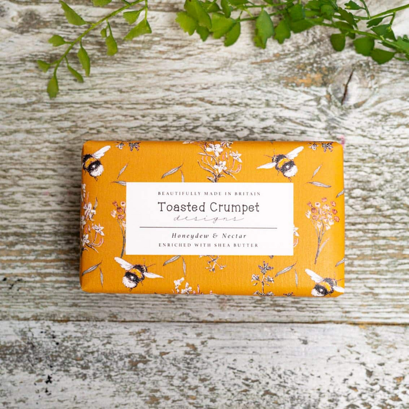 Bar of soap with decorative packaging featuring bees and flowers on a wooden surface.
