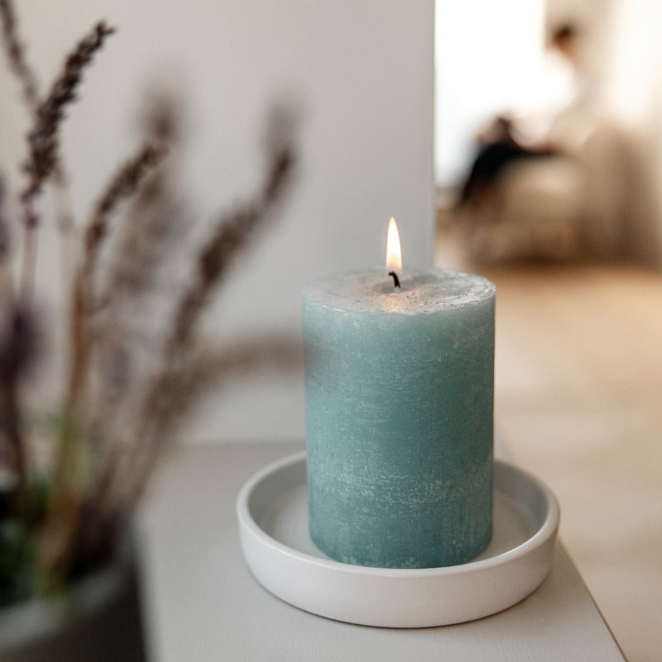 Sea blue pillar candle on a white plate with blurred background