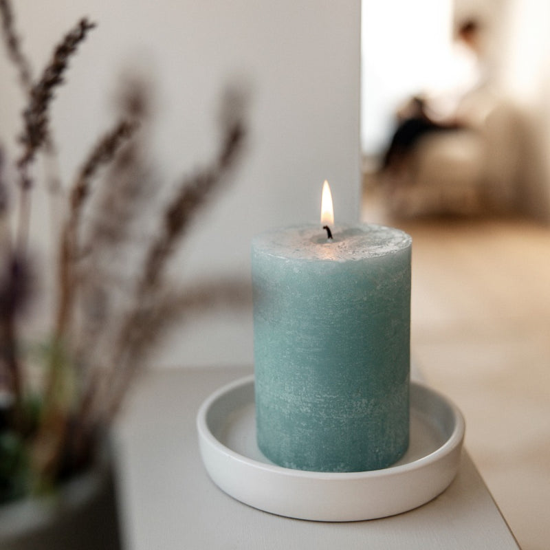 Sea blue pillar candle on a white plate with blurred background