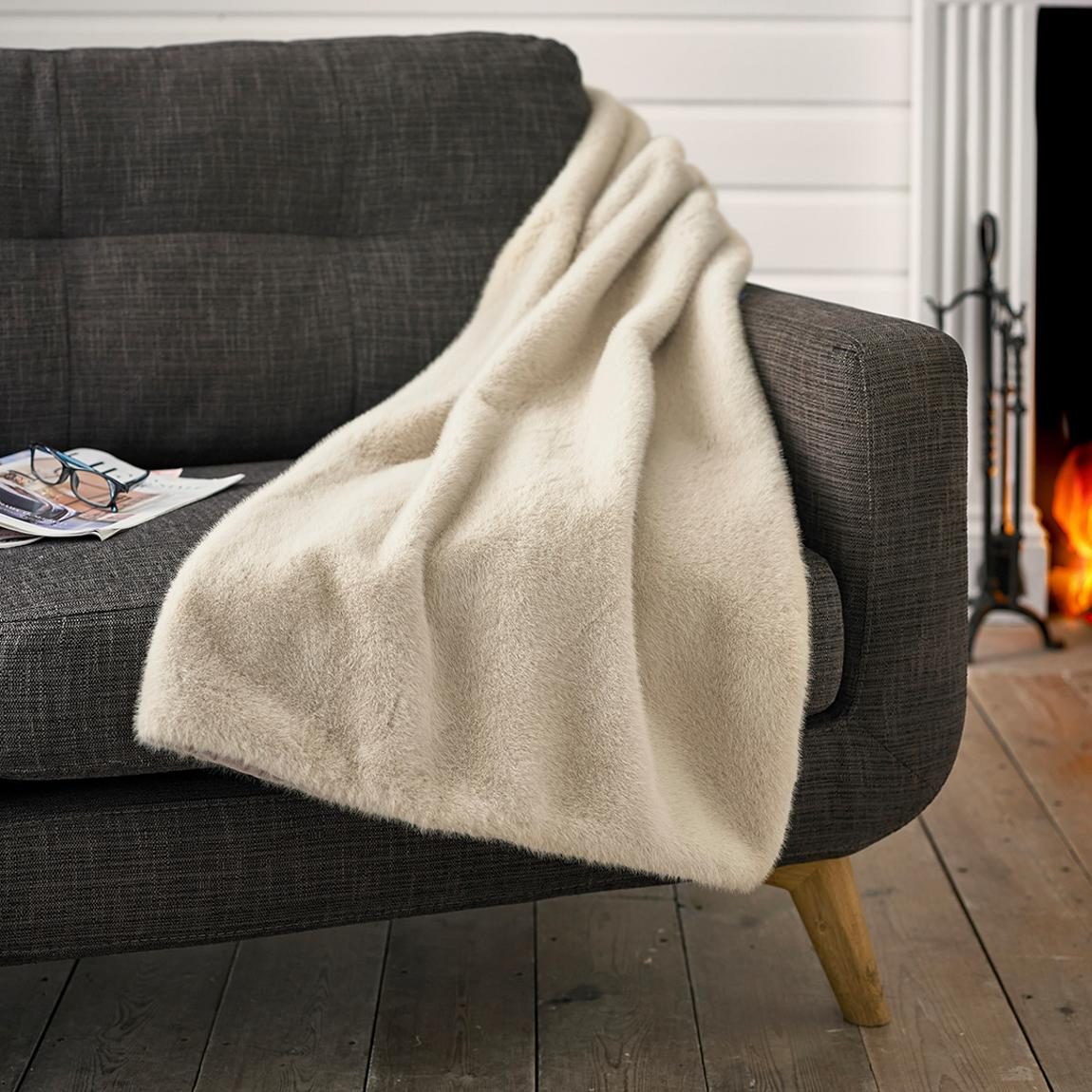 Beige blanket draped over a gray sofa in a cozy living room with a fireplace.