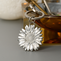 Silver sunflower-shaped keychain on a gray surface with a blurred background