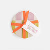 Round gift box with a colorful ribbon and 'caroline gardner' tag on a white background
