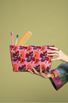 Person holding a floral toiletry bag with toothbrush and comb on a green background
