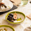 Green ceramic bowl with figs on a patterned tablecloth