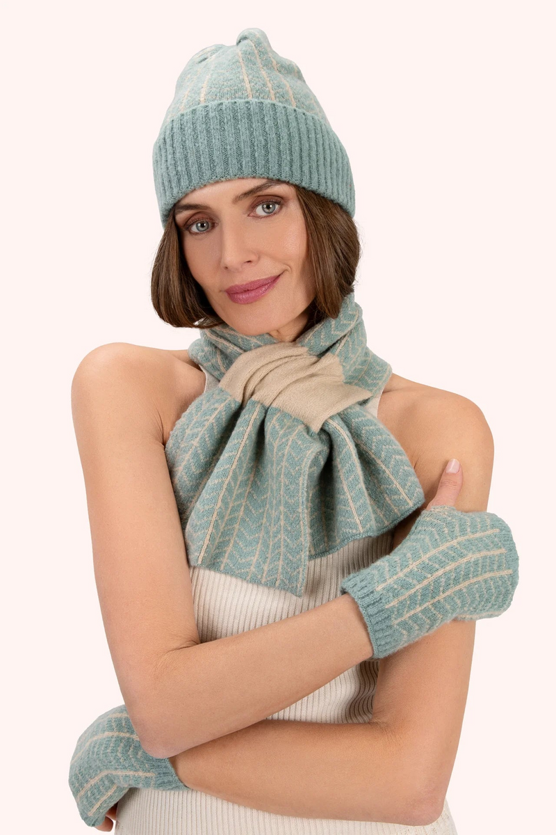 Woman wearing a matching teal knit hat, scarf, and gloves on a white background