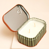 Striped candle in a tin with a lid on a beige background
