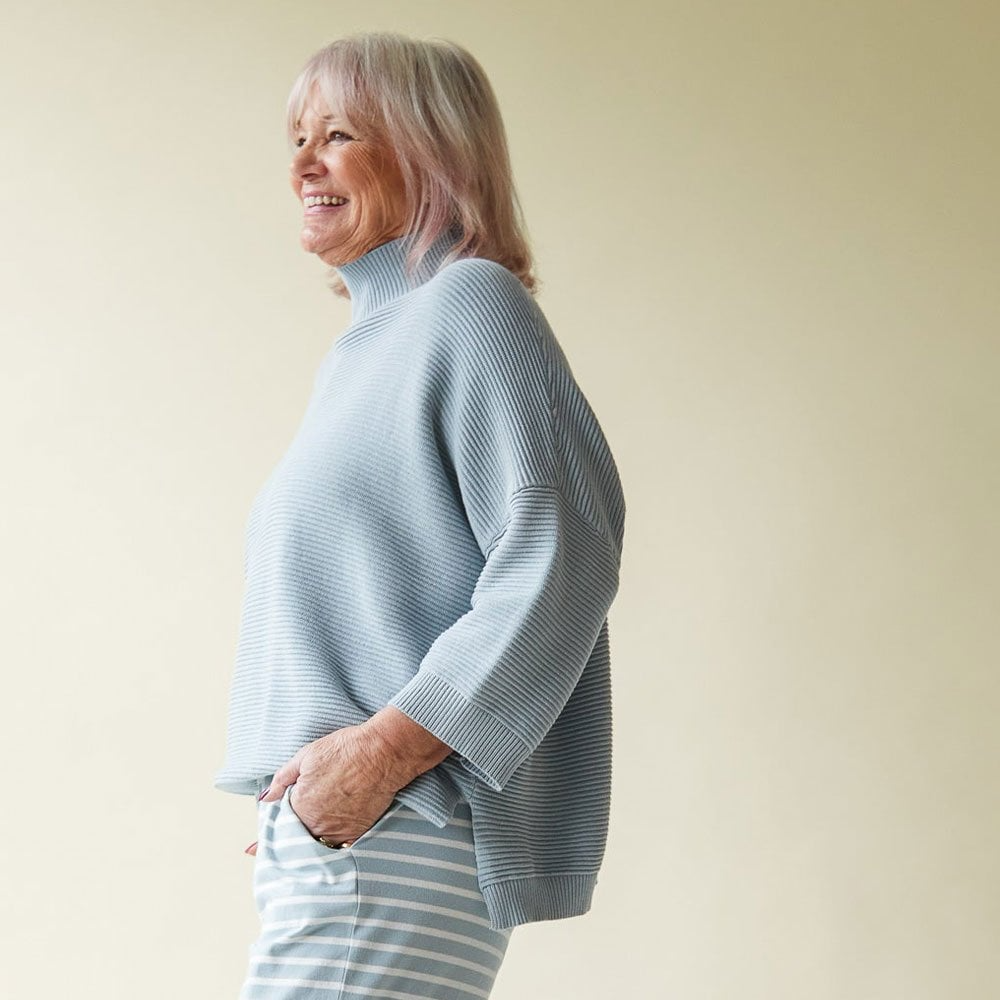 Woman wearing a light blue sweater and striped pants against a plain background